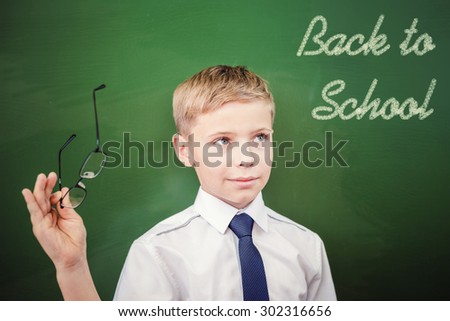 Handsome schoolboy looking to blackboard with text of back to school, at classroom. Little boy dressed in white shirt and holding glasses. Concept of knowledge day and first of september