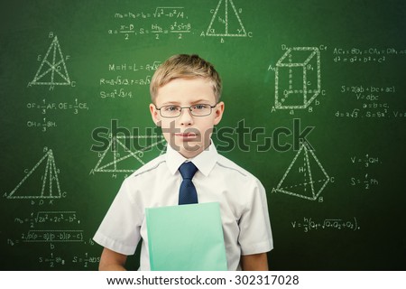 Smart student or schoolboy with a notebook, dressed in school uniform and sunglasses standing near blackboard scribbled with chalk - formulas and drawing. Concept of intelligent and scientist boy
