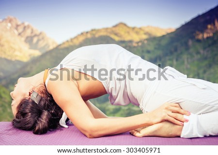Young caucasian woman doing yoga at mountain, dressed in white sportswear. She relaxing and meditating at top of summit at yoga mat. Kazakhstan, Almaty, Medeo. Selective focus on the hands