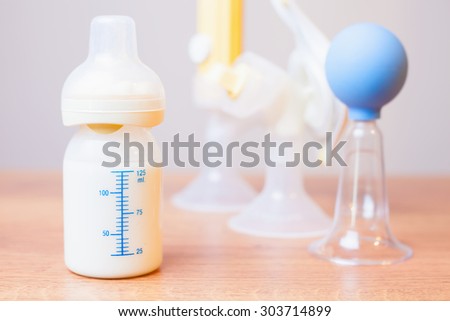 Baby bottle with milk and a measuring scale, manual breast pump, mothers breast milk is the most healthy food for newborn baby. Objects standing in a row. Selective focus