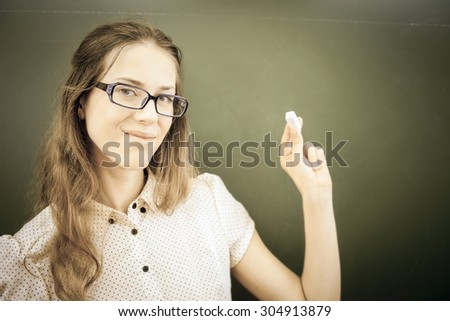 beautiful young woman - teacher or student, holding a chalk near green chalkboard at classroom at university ar school