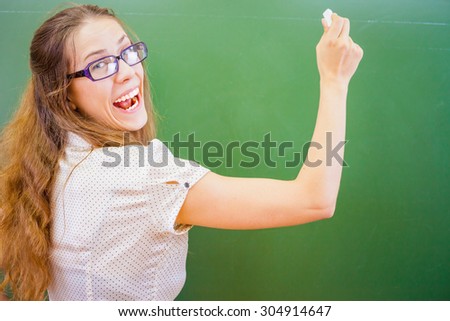 Funny and happy teacher or student wrote on blackboard with chalk at classroom at school or university. She looking at the camera and wearing glasses. Maybe she has gone mad