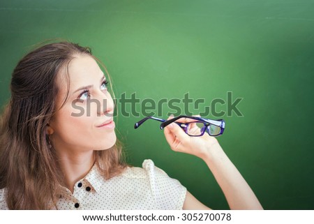 Pretty teacher or student holding glasses and looking up to blackboard with copy space for design and any text. Indoor at classroom at school or university.