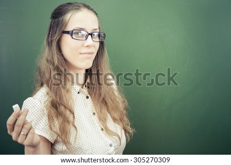 beautiful young woman - teacher or student, holding a chalk near green chalkboard at classroom at university ar school. Let\'s go to the blackboard!