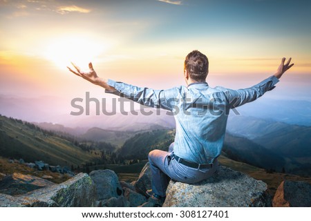 Image of a young businessman who sits on the top of the mountain and man feels good and imagines himself almighty