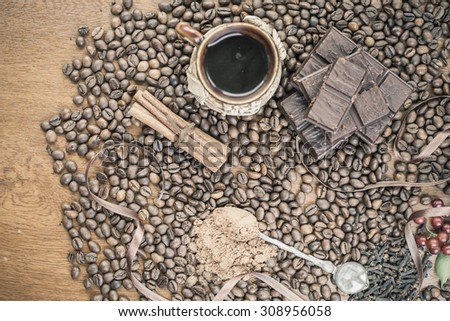 For holiday of chocolate day - wooden table background decorated a lot of coffee beans, chocolate bar, a cup of hot coffee, cacao, cinnamon.