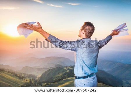 Image of a happy successful businessman who standing on the top of mountain and holding document paper. He looks into distance, thinking about future plans. Concept of professional career