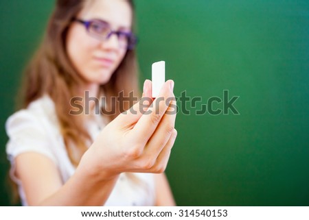 beautiful young woman - teacher or student, holding a chalk near green chalkboard at classroom at university ar school. Let\'s go to the blackboard!