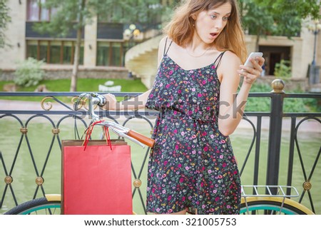Surprised caucasian woman with bugs using mobile phone or typing sms, near vintage bicycle. Her summer vacation in Italy, Milan for shopping and fun!