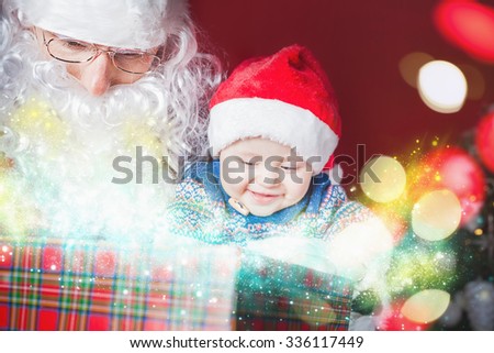 Christmas baby wearing a Santa Claus hat and Santa opening a present and gift box! Night, xmas eve, surprise. Magical light. Design. New Year
