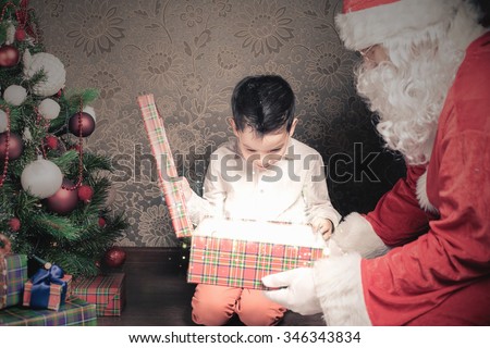 Happy shocked boy surprised to see Santa Claus! Looking at gift box. Child dressed in red Santa hat. Surprise! Xmas and New Year holiday. Your dad dressed in Santa Claus costume! Christmas inspiration