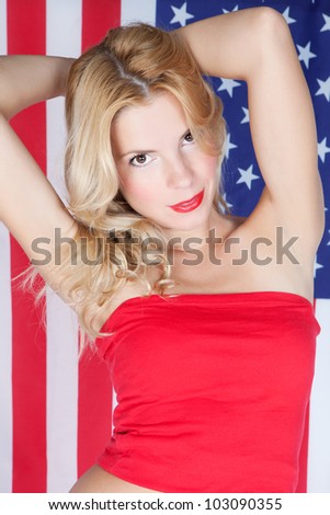 Beautiful young woman with blonde long hair on the background of the American flag