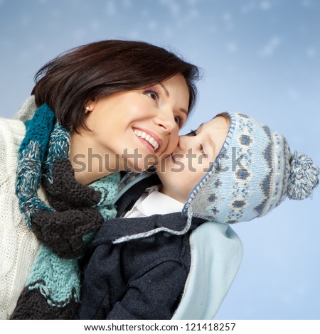 Happy family in winter clothing. Little son kissing his happy smiling mother on a cheek over blue