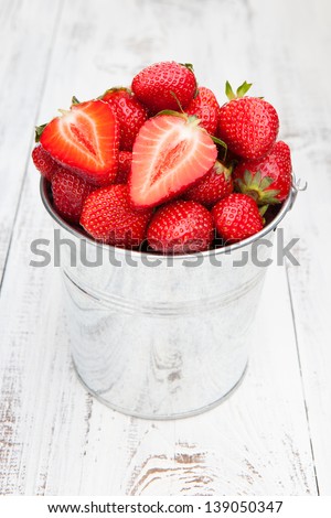 Juicy fresh strawberries in a bucket on a white wooden background