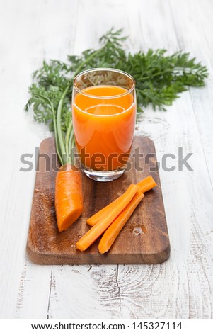 Carrot juice in glass with fresh organic carrots on white wooden table