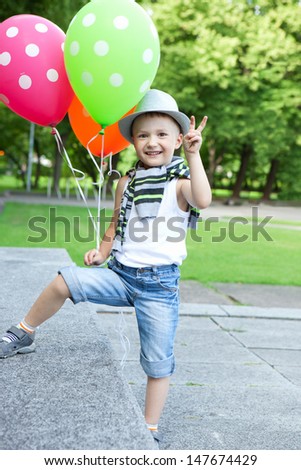 Funny little boy playing with balloons in a green summer park