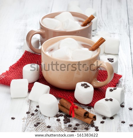 Mugs of hot chocolate with marshmallows and cinnamon sticks on a white wooden background