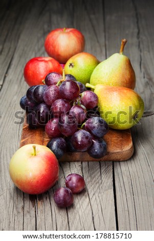Harvested grapes with red apples, ripe pears and plums on dark wooden background