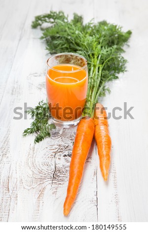 Carrot juice in glass with fresh organic carrots on white wooden table