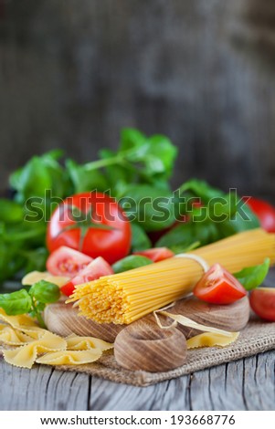 Spaghetti and tomatoes with herbs on a dark and vintage wooden table, selective focus