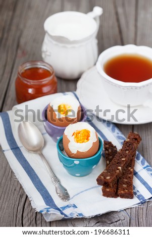 Healthy breakfast with boiled eggs, milk and cup of tea on dark wooden background, selective focus