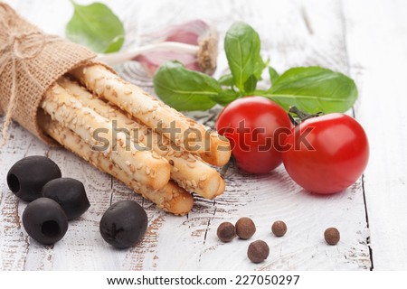 Grissini bread sticks with sesame, olives and basil on white wooden background