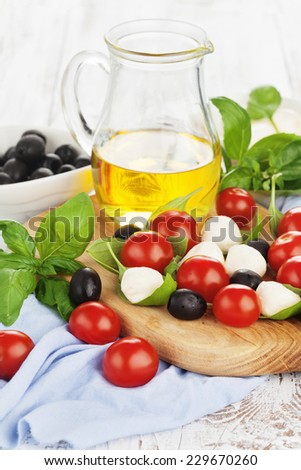 Fresh cherry tomatoes, mozzarella, olive oil and basil on white wooden background, selective focus