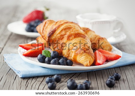 Delicious breakfast with fresh croissants and ripe berries on old wooden background