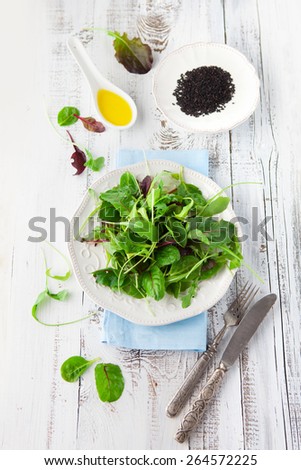 Fresh green salad with spinach, arugula, romaine and lettuce and sesame seeds on a rustic white background, top view