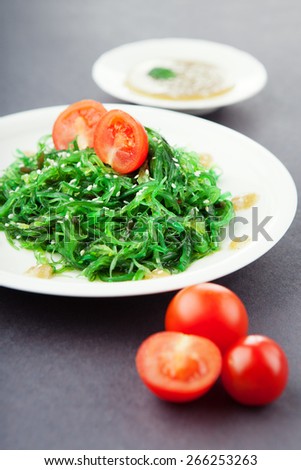 Pickled seaweed with nut sauce, garnished with sesame seeds and cherry tomatoes, black background