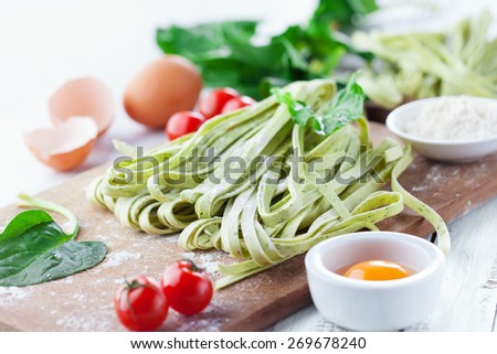 Fresh pasta tagliatelle with spinach leaves, vegetables and eggs on white wooden background, selective focus
