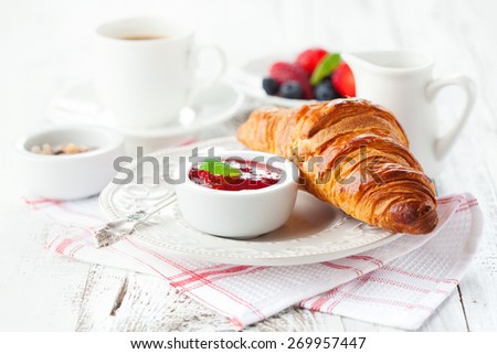 Breakfast with fresh croissants, cup of coffee and strawberry jam on a white wooden background, selective focus