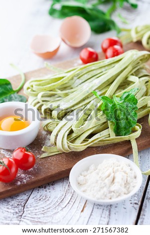 Fresh pasta tagliatelle with spinach leaves, vegetables and eggs on white wooden background, selective focus