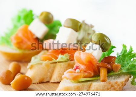 Bruschettas with cheese, smoked salmon and salad on crusty bread on white wooden background, selective focus