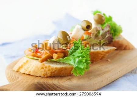 Bruschettas with cheese, smoked salmon and salad on crusty bread on white wooden background, selective focus