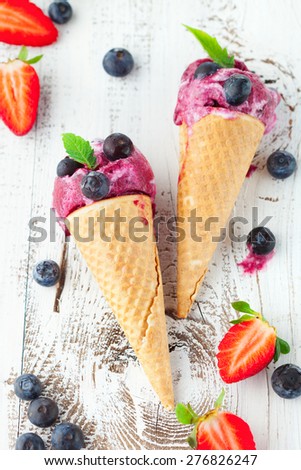 Homemade berry ice cream cones with mint leaves and fresh blueberries on white wooden background, top view