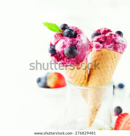Homemade berry ice cream cones with mint leaves and fresh blueberries on white wooden background, selective focus