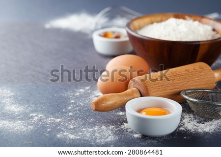 Ingredients and tools for baking - flour, eggs and rolling pin on the black background, selective focus