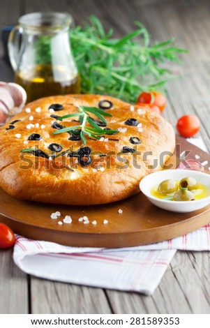 Freshly baked traditional Italian focaccia bread with rosemary and black olives on old wooden background, selective focus