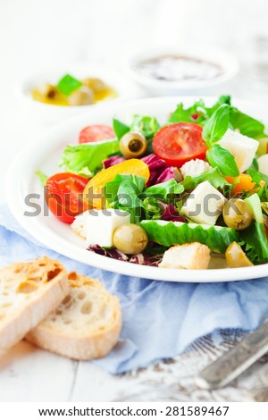 Fresh summer salad with cherry tomatoes, spinach, green olives and goat cheese in a plate on white wooden background, selective focus