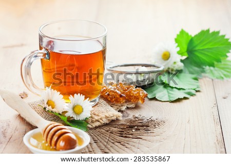Herbal tea in a glass bowl with camomile flowers and honey on rustic wooden background, selective focus