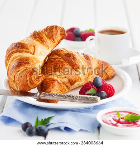 Breakfast with cup of coffee, fresh croissants and ripe berries on white wooden background, selective focus