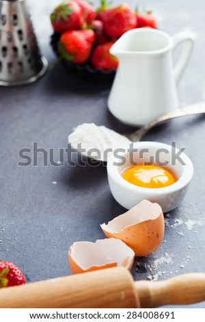 Ingredients and tools for baking - flour, eggs, rolling pin and fresh berries on the black background, selective focus