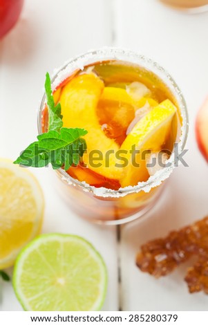 Glass of ice tea with lemon, peach, ice cubes and fresh mint on rustic white wooden background, top view
