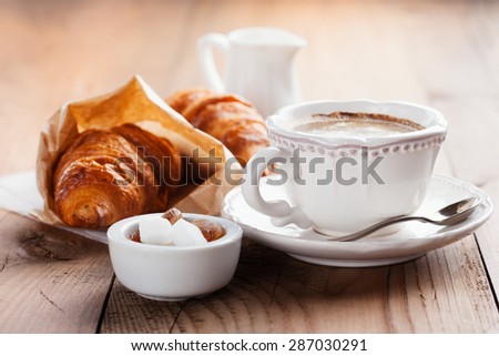 Crispy fresh croissants and cup of coffee espresso on a rustic wooden background, morning breakfast, selective focus