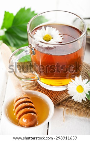 Herbal tea in a glass bowl with camomile flowers and honey on white rustic wooden background, selective focus