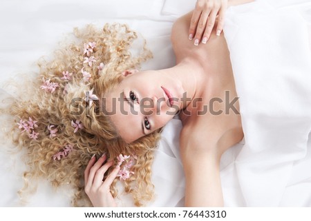 Picture of happy woman with pink flowers in blonde hair lying on the white bed