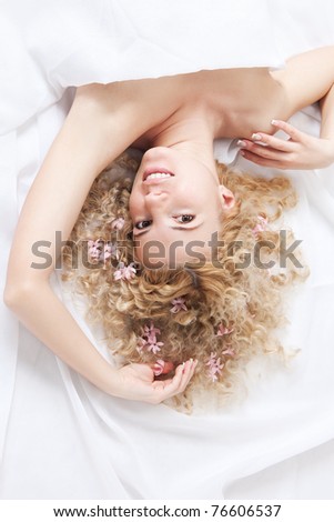 Picture of happy woman with pink flowers in blonde hair lying on the white bed