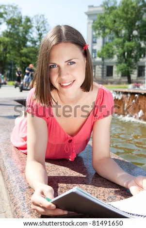 Smiling young brunette woman holding a book outdoors