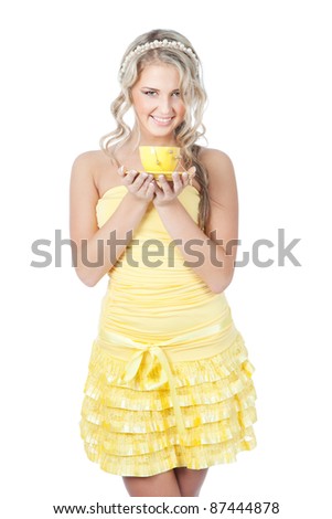 Beautiful young blonde woman in yellow dress holding yellow cup, white background